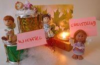 Drei Wichtel und das Christkind gruppieren sich andächtig vor einer Kerze. 